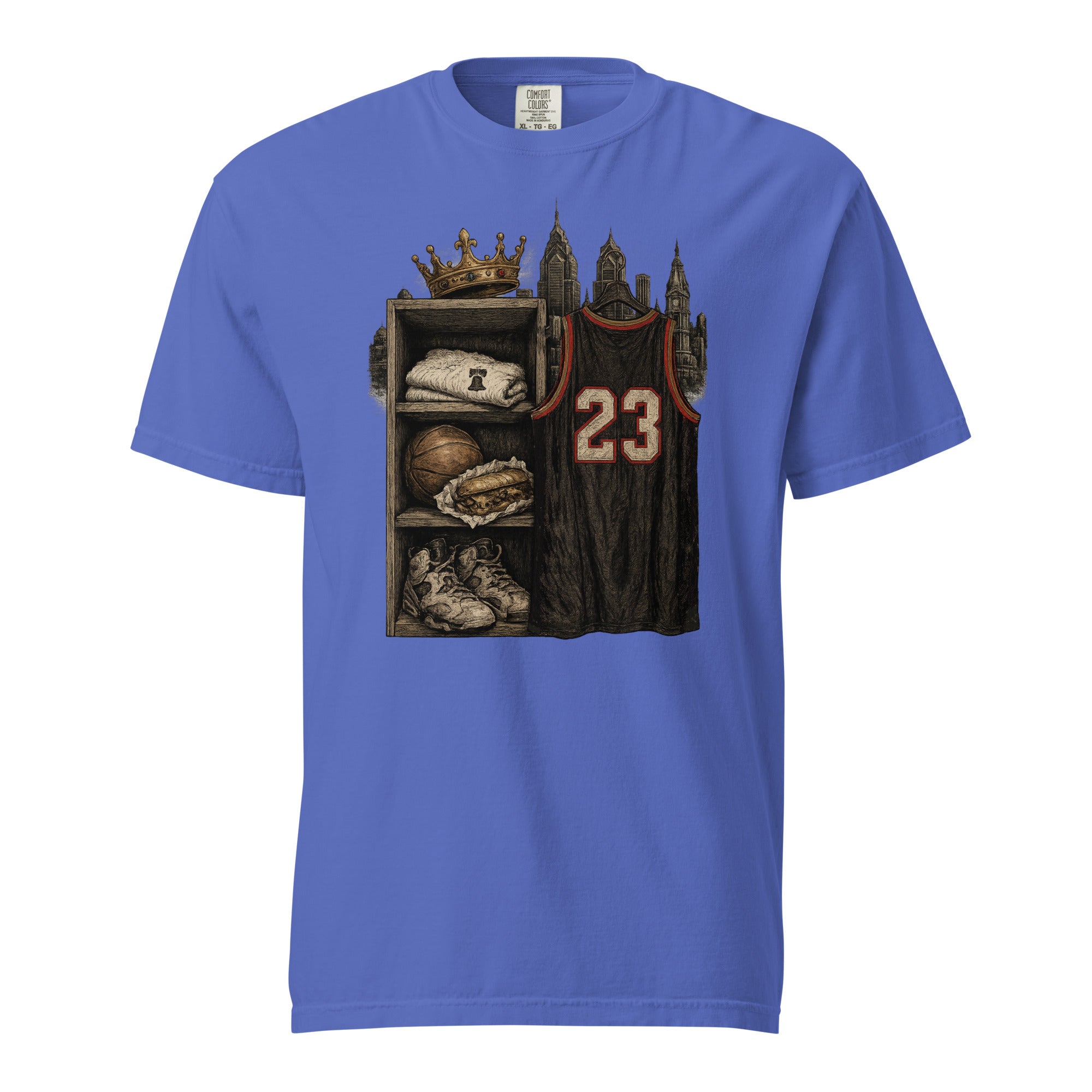 A royal blue short-sleeve crewneck t-shirt featuring a detailed graphic print on the front. The graphic depicts a dark locker shelf with a baseball cap, a basketball, a baseball bat, and sneakers, topped with a gold crown, next to a dark brown sports jersey with the number 23.