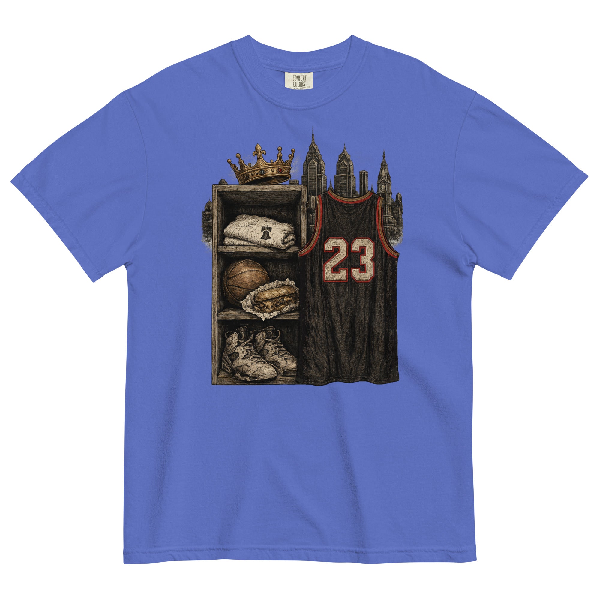 A royal blue short-sleeve t-shirt with a detailed graphic print on the front. The graphic shows a basketball-themed shelf with a crown, a folded sweatshirt, a basketball, sneakers, and a dark basketball jersey with the number 23.