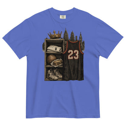 A royal blue short-sleeve t-shirt with a detailed graphic print on the front. The graphic shows a basketball-themed shelf with a crown, a folded sweatshirt, a basketball, sneakers, and a dark basketball jersey with the number 23.